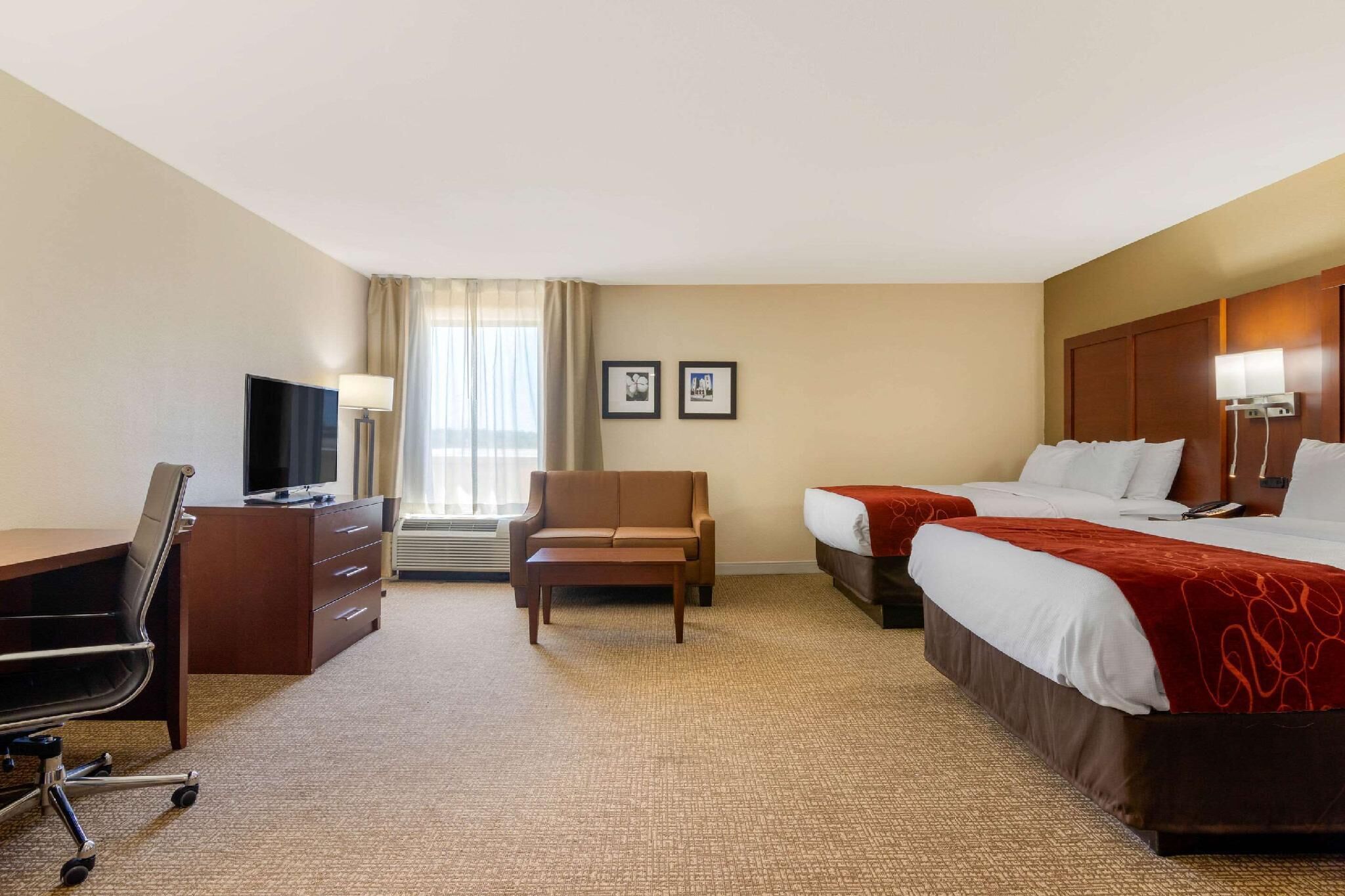 A hotel room with a desk, chair, two beds, a TV, and a sofa.