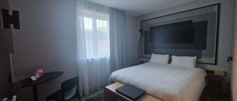 Una habitación de hotel con una cama, un escritorio, una silla y un ventanal grande.
