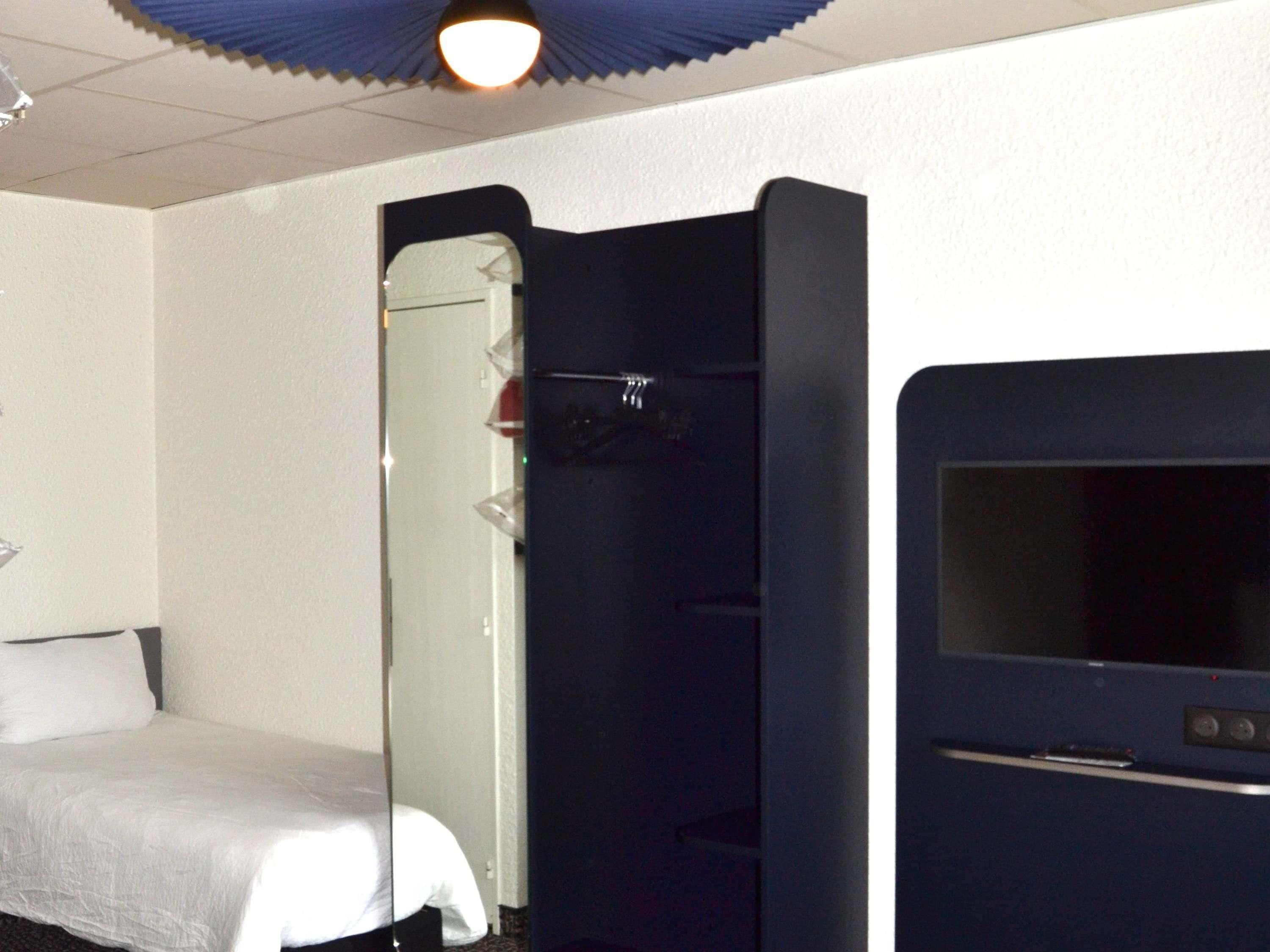 A hotel room with a bed, a mirror, a wardrobe, and a television.