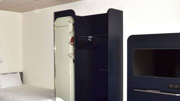A hotel room with a bed, a mirror, a wardrobe, and a television.