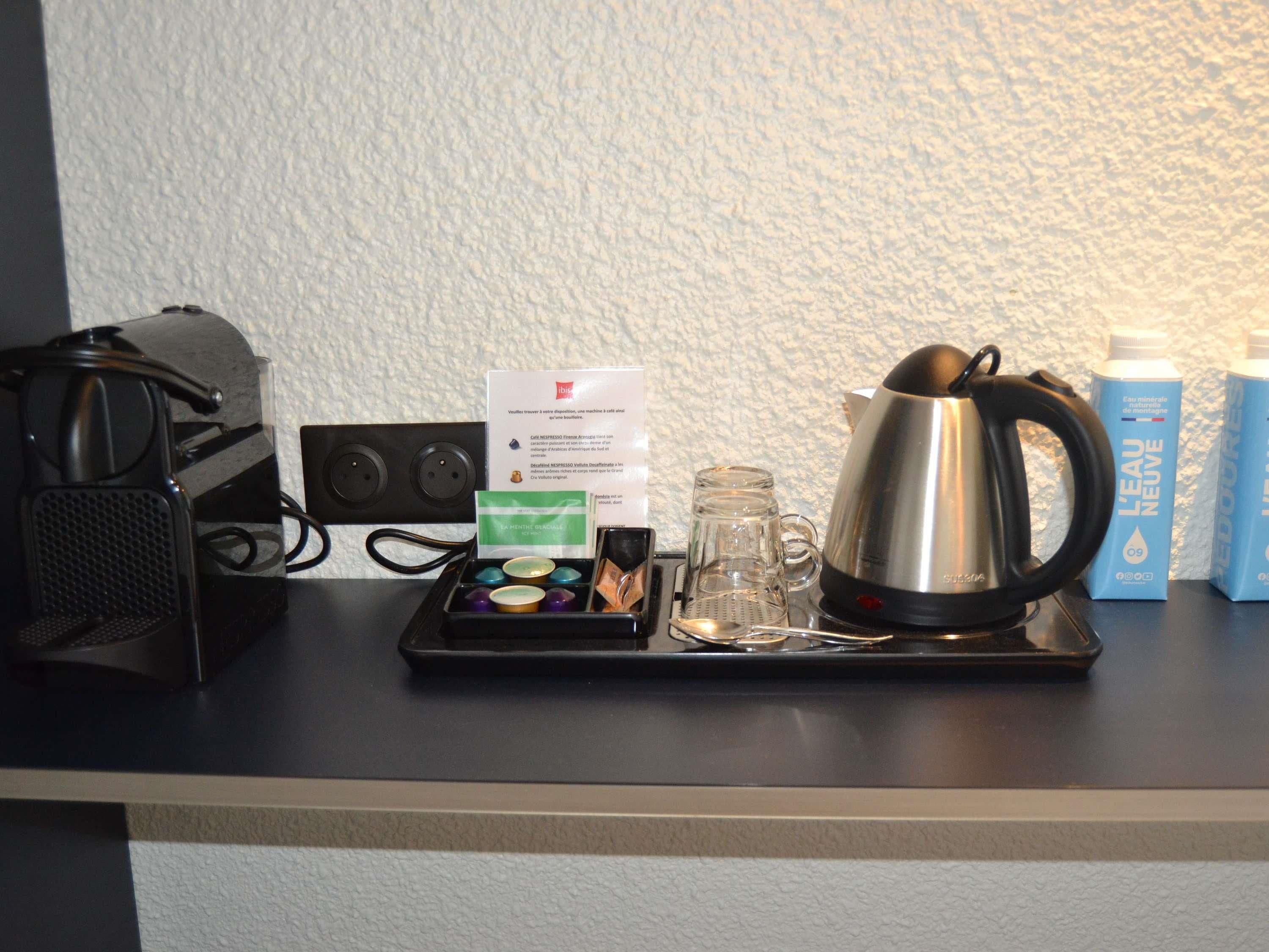 A coffee station with a coffee maker, a glass carafe, a tray with coffee pods and a glass, and bottled water.