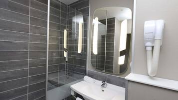 A modern bathroom with a glass shower enclosure, a white sink, a large mirror, and a hairdryer mounted on the wall.
