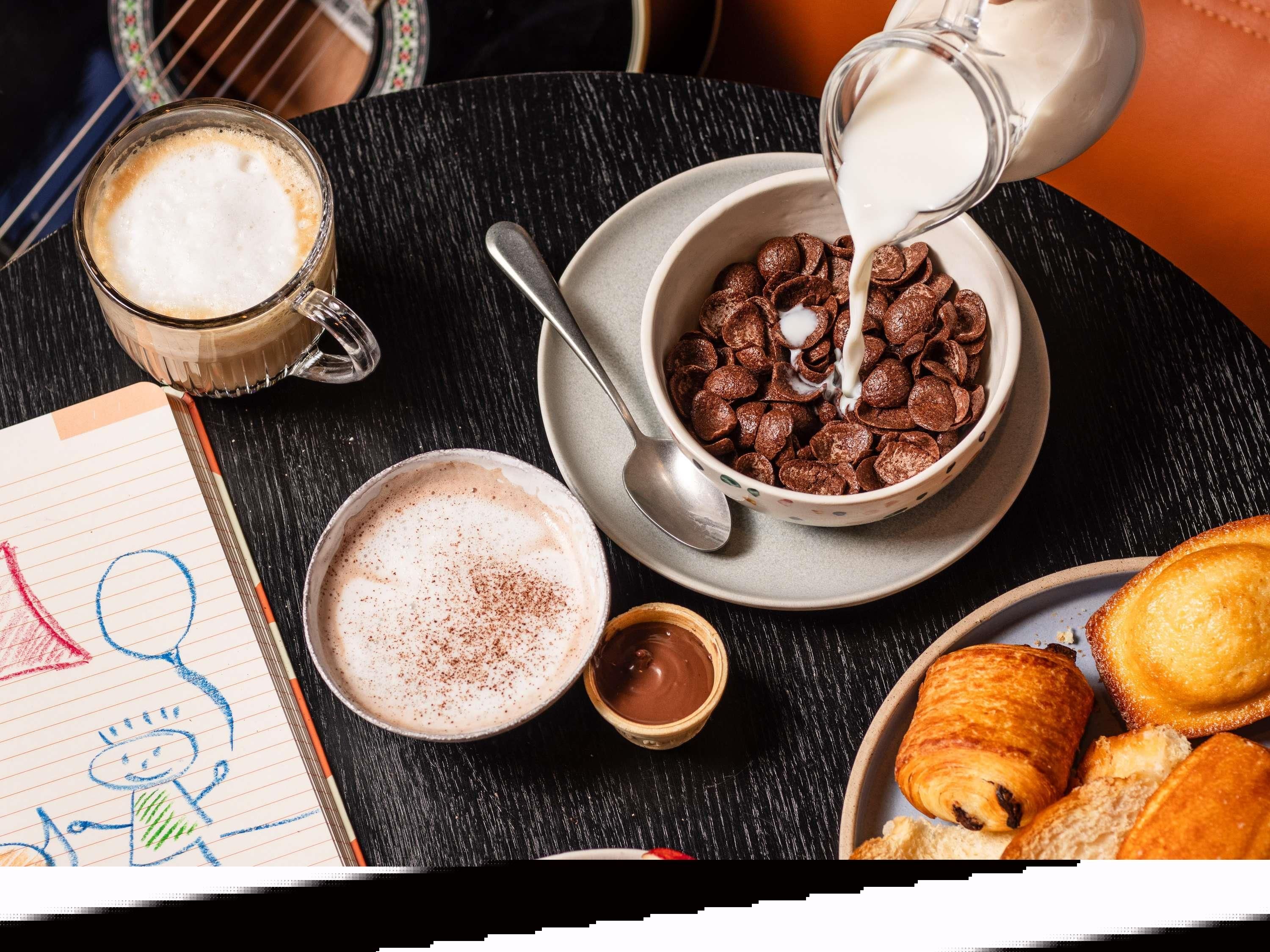 Mesa com café da manhã: cereais, leite, café e pães.