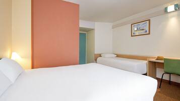 Een hotelkamer met twee bedden, een bureau, een stoel en een schilderij aan de muur.