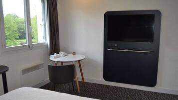 A hotel room with a bed, a small round table with a telephone and tissues, a TV mounted on the wall, and a window with curtains.