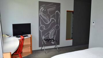 Habitación de hotel con cama, escritorio con televisor, silla, cuadro en la pared y puerta.