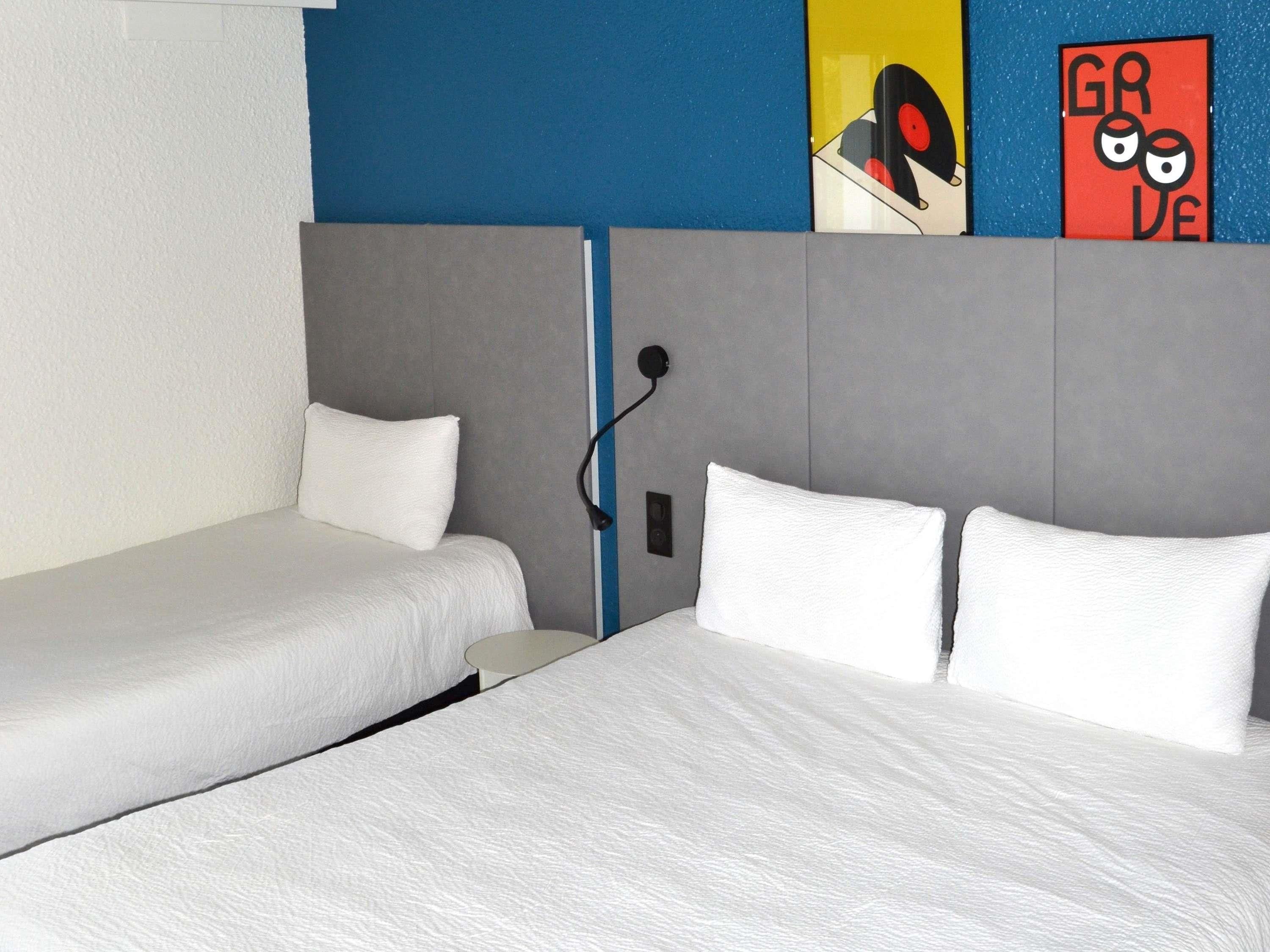 Una habitación de hotel con dos camas individuales, un cabecero gris y una pared azul decorada con obras de arte.