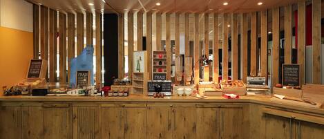 A wooden counter with various food items and a coffee machine, surrounded by vertical wooden slats.