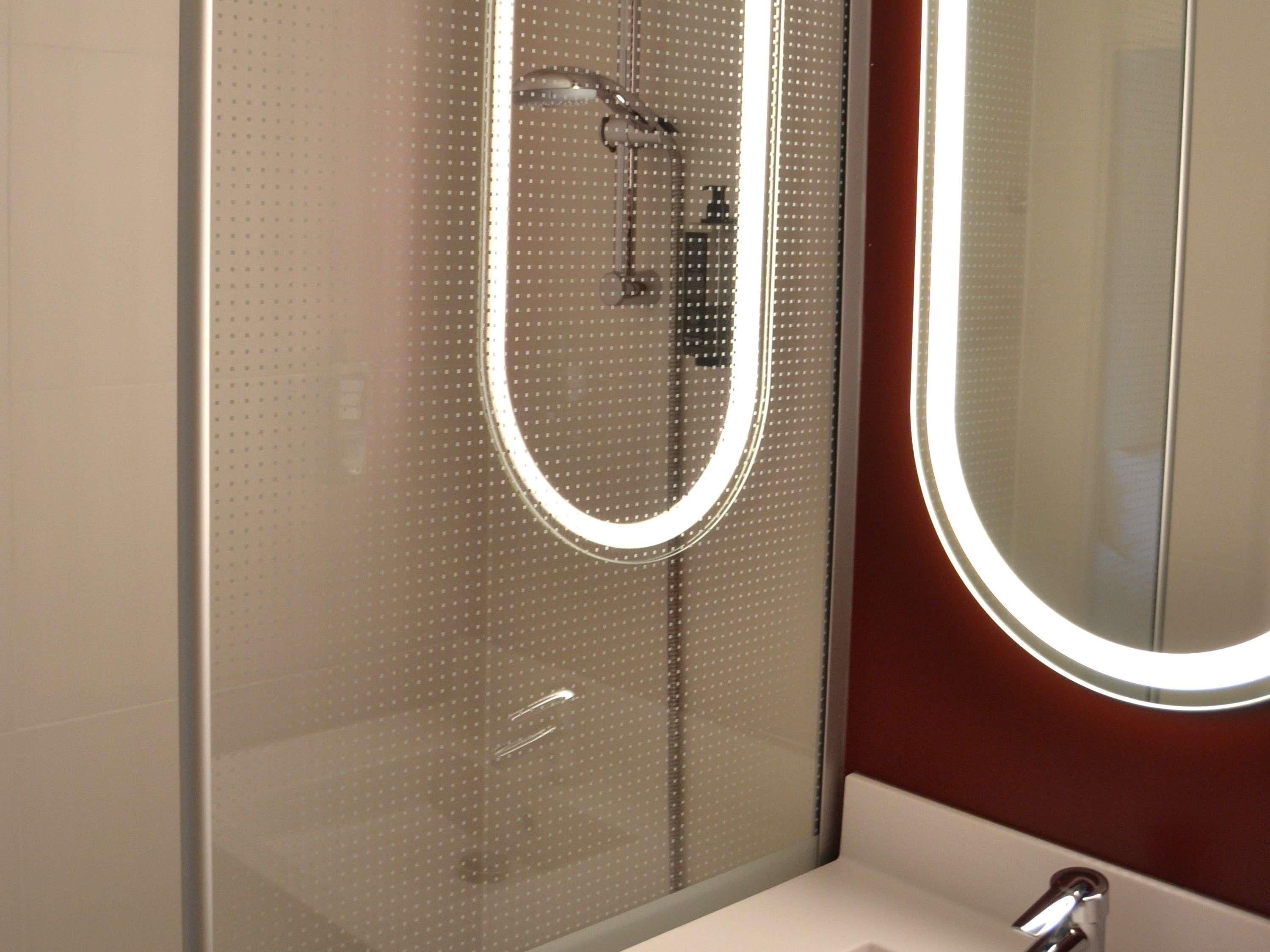 Un baño con cabina de ducha de vidrio, un lavabo blanco y un espejo con luz circular.