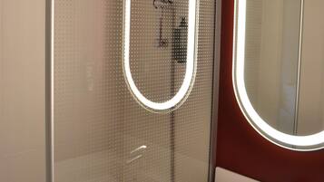 Un baño con cabina de ducha de vidrio, un lavabo blanco y un espejo con luz circular.