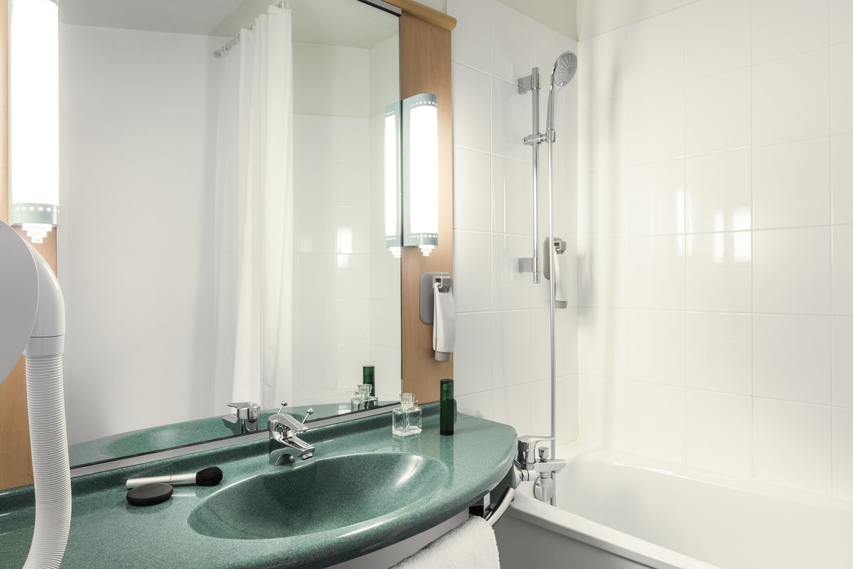 Een moderne badkamer met een groene wastafel, een spiegel, een handdouche en een witte badkuip.