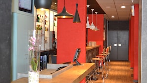 A bar area with a wooden counter, hanging pendant lights, and a red accent wall. - ibis Egletons (Egletons)