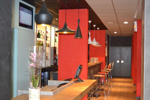 A bar area with a wooden counter, hanging pendant lights, and a red accent wall.
