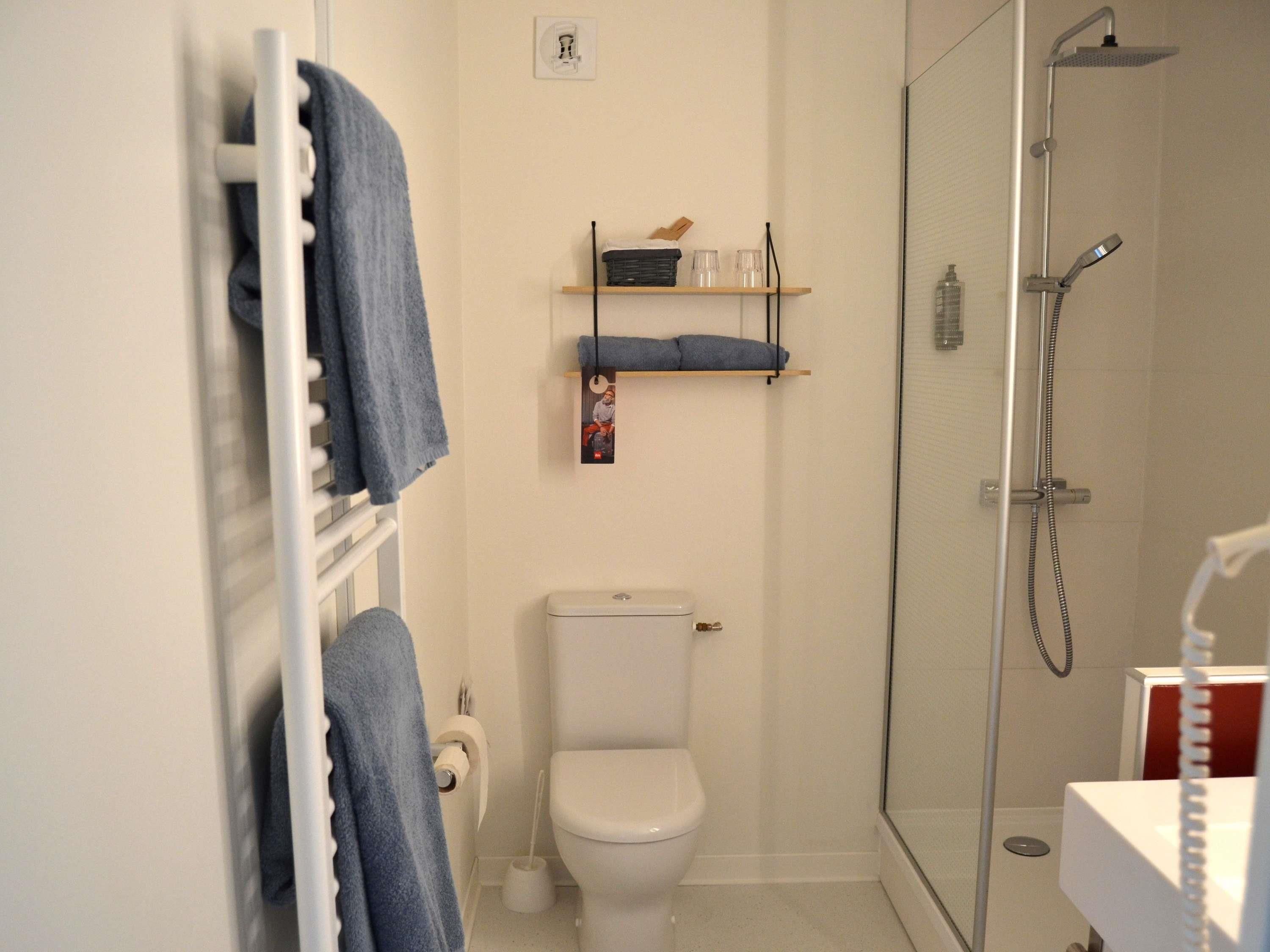 A bathroom with a toilet, a shower, a towel rack, and a shelf with toiletries.