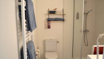 A bathroom with a toilet, a shower, a towel rack, and a shelf with toiletries.