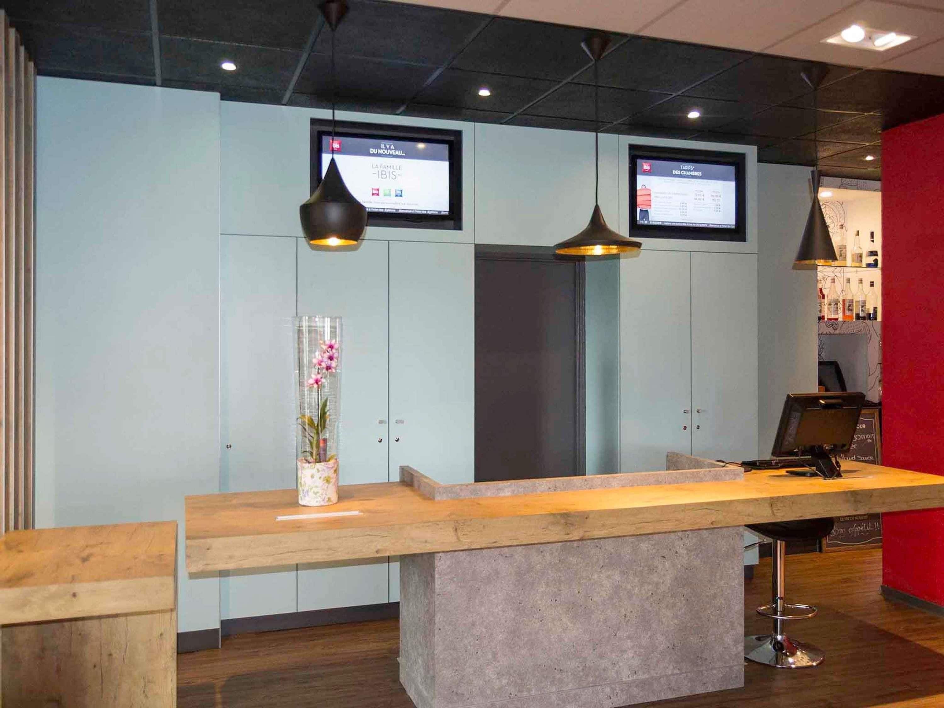 A reception desk with two monitors, a vase with flowers, and a bar area in the background.