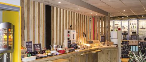 A modern bar area with wooden accents, a counter with various items, and a display of bottles.