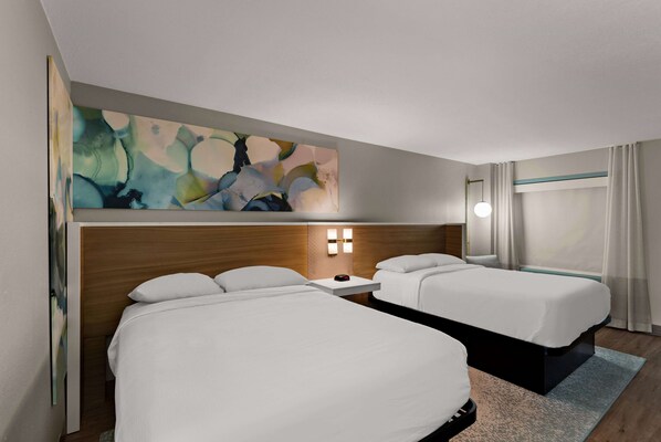 Habitación de hotel con dos camas, cabecero de madera, un cuadro y una ventana con cortinas.