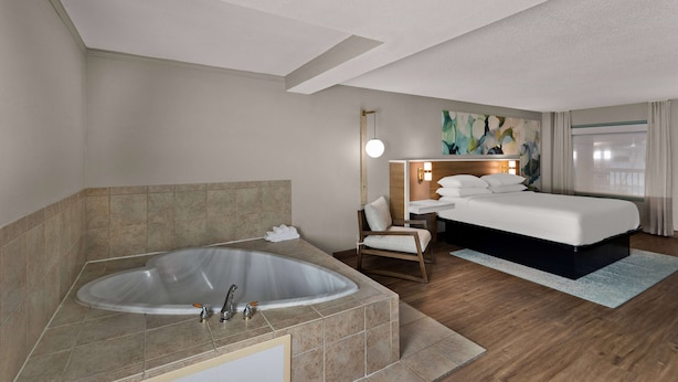 A hotel room with a large bathtub, a bed, a chair, and a painting on the wall. - Wyndham Garden Ankeny/Des Moines (Ankeny)
