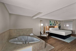 Habitación de hotel con una bañera grande, una cama, una silla y un cuadro en la pared.