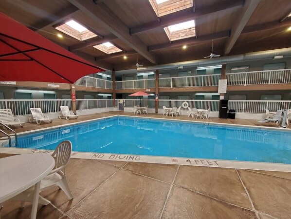 Una piscina interior con varios niveles de balcones, barandillas blancas y un paraguas rojo.