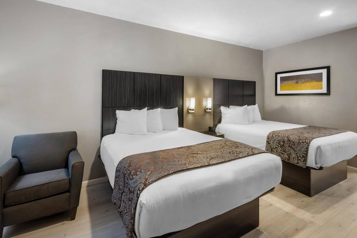 A hotel room with two beds, a chair, and a framed picture on the wall.