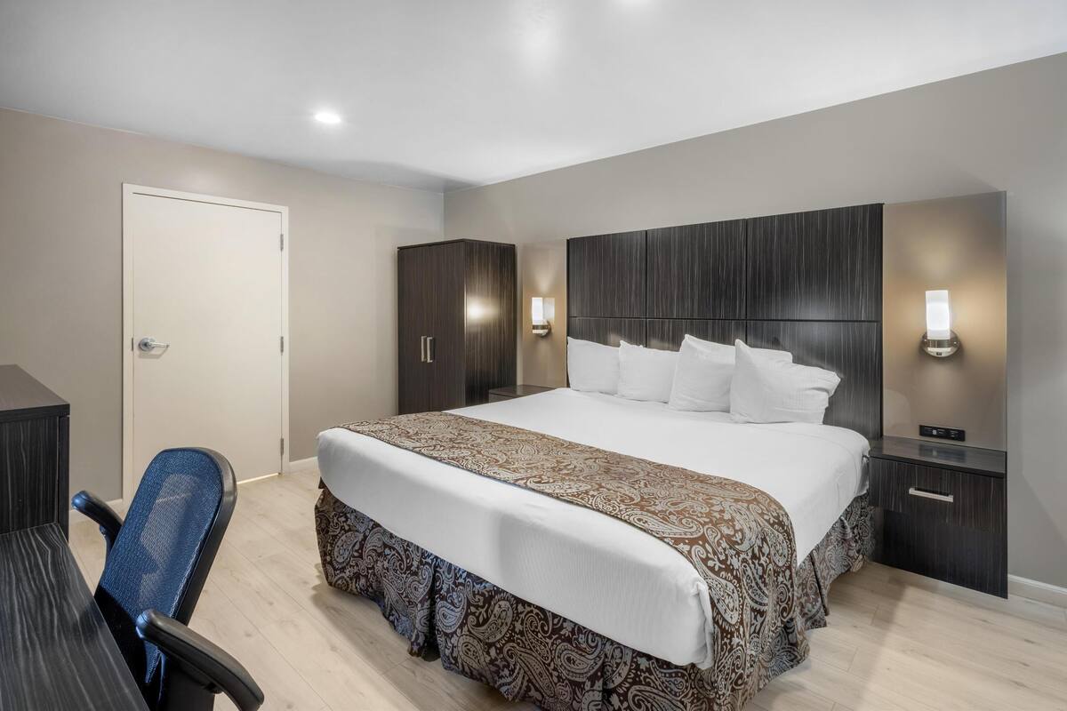 A hotel room with a large bed, a desk, a chair, and two bedside tables with lamps.