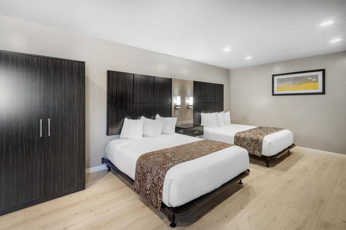 A modern hotel room with two beds, a large wardrobe, and a painting on the wall.