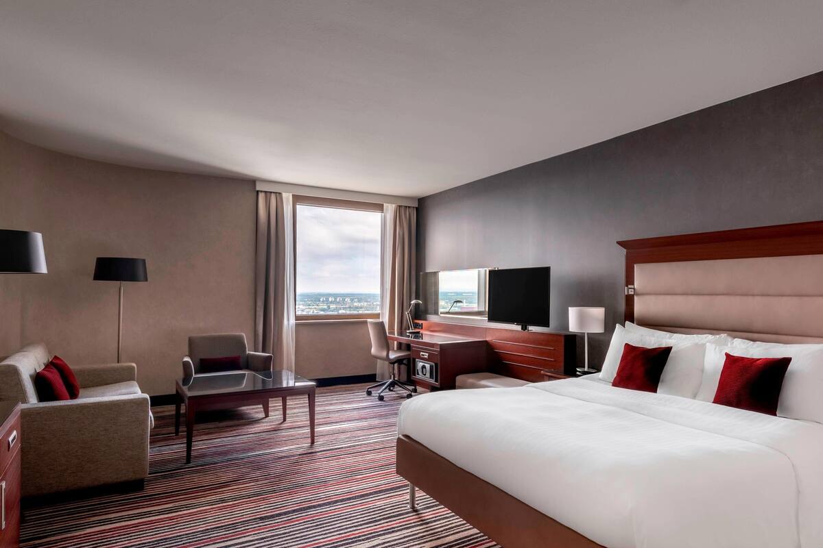 Een hotelkamer met een groot bed, een bureau, een stoel, een televisie en uitzicht op de stad.