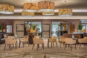 Eine Hotelhalle mit mehreren Sitzbereichen, einer Bar und großen Fenstern.