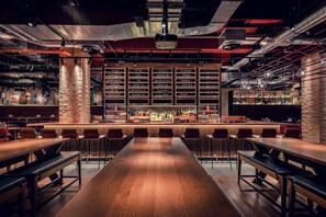 Zona de bar con una larga mesa de madera y varios taburetes, rodeada de estanterías llenas de botellas.