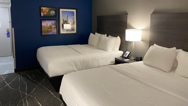 A hotel room with two beds, a nightstand with a lamp, and framed pictures on the wall.