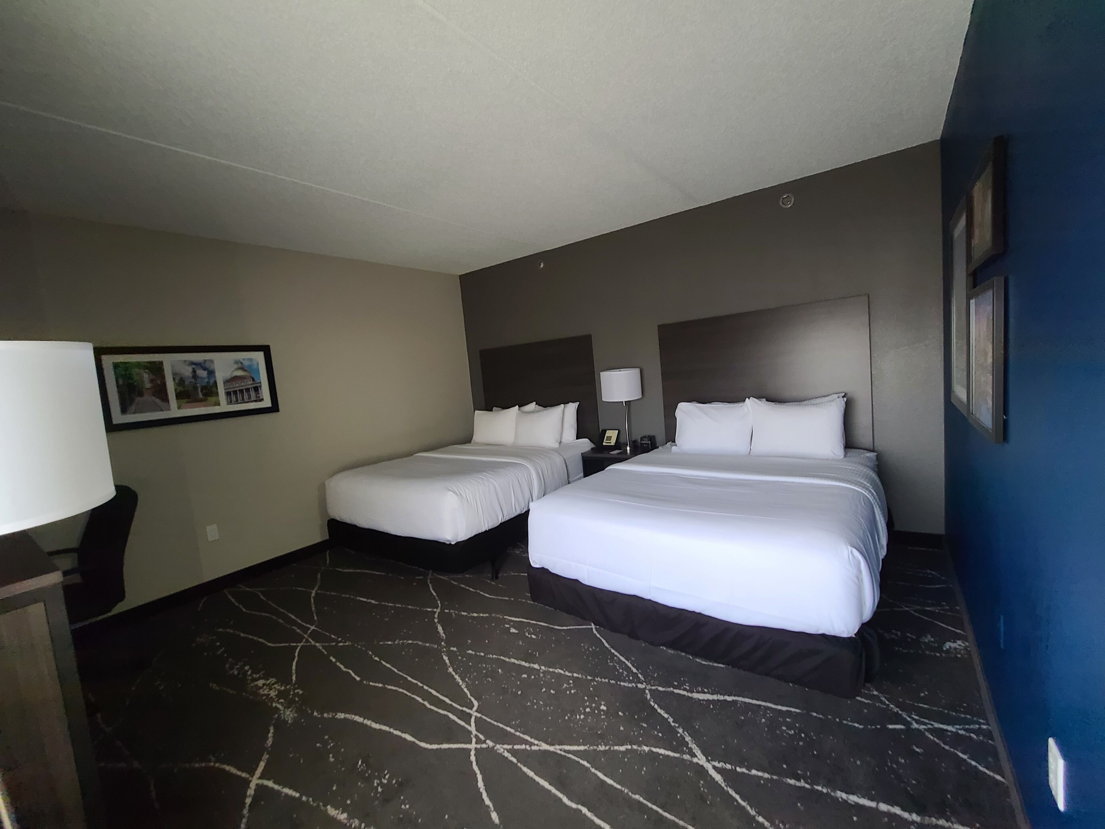 Una habitación de hotel con dos camas, una mesita de noche, una lámpara y un cuadro en la pared.