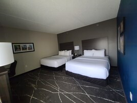 Una habitación de hotel con dos camas, una mesita de noche, una lámpara y un cuadro en la pared.