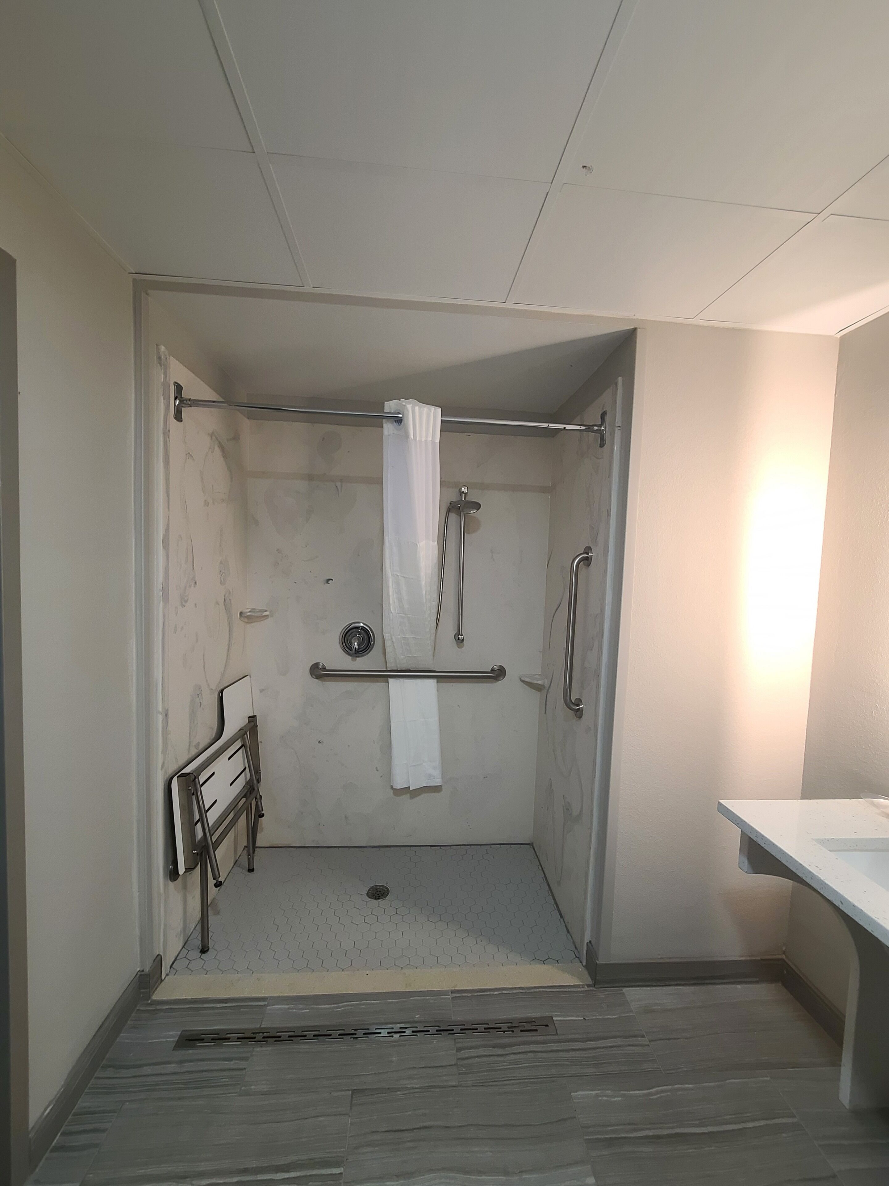 A small, enclosed shower area with a white shower curtain, grab bars, and a towel rack.