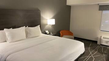 A hotel room with a large bed, a bedside lamp, a chair, and a window.