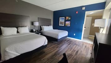 A hotel room with two beds, a desk, a chair, and a door leading to a bathroom.