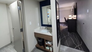 A hotel bathroom with a sink, mirror, and a trash bin.