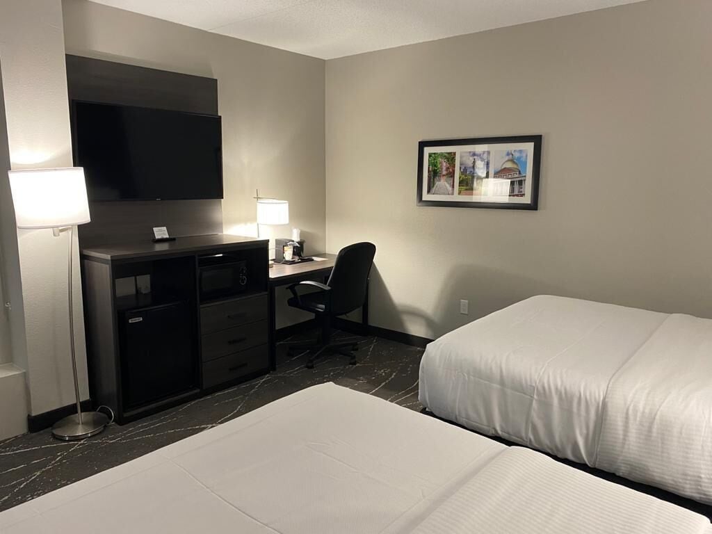 A hotel room with a desk, chair, two beds, a TV, and a framed picture on the wall.