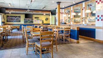 A restaurant interior with multiple wooden tables and chairs, a pool table, and a counter with a menu display.