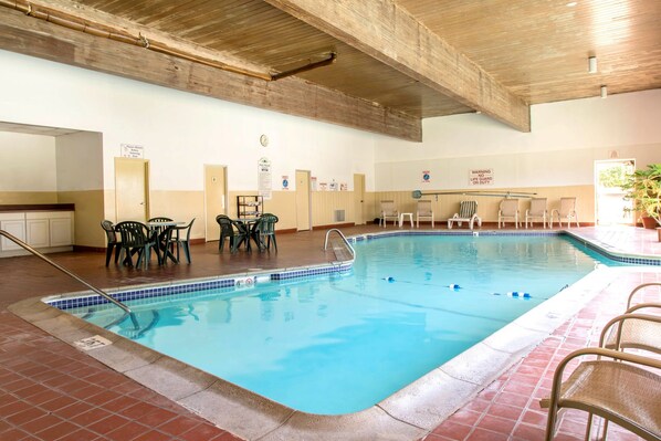 An indoor swimming pool with a tiled edge, surrounded by lounge chairs and a table with chairs.