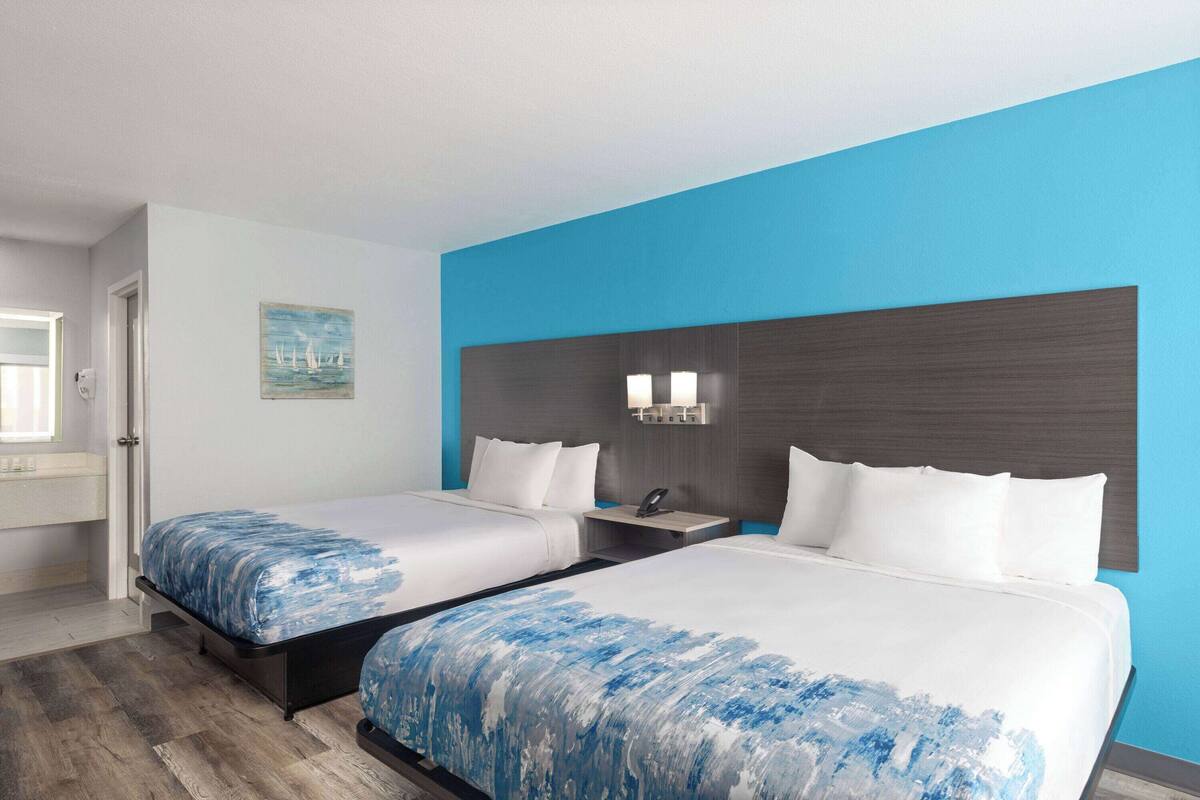 Habitación de hotel con dos camas, una mesita de noche, una lámpara de pared y una ventana con vistas.