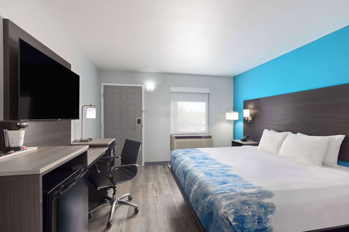 Una habitación de hotel con cama, escritorio, silla, televisor y ventana.