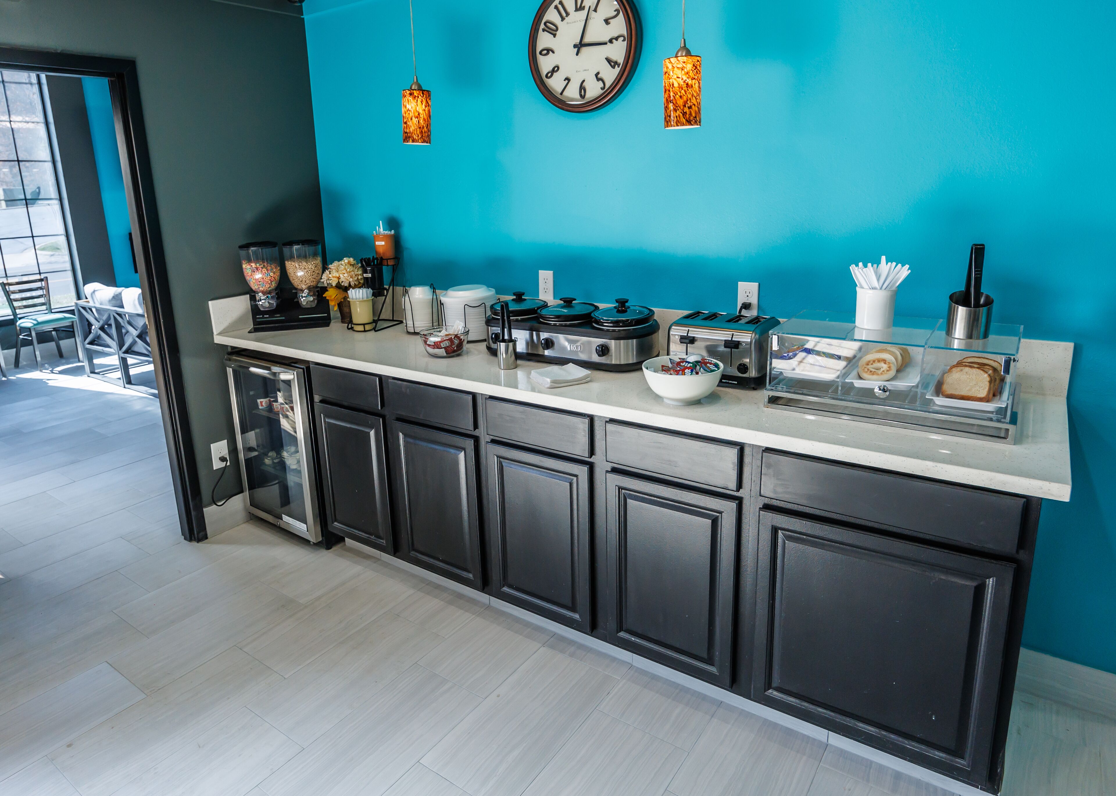 A modern kitchen with a teal accent wall, a large clock, and various appliances like a toaster and coffee maker.