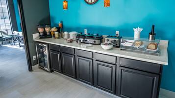 A modern kitchen with a teal accent wall, a large clock, and various appliances like a toaster and coffee maker.
