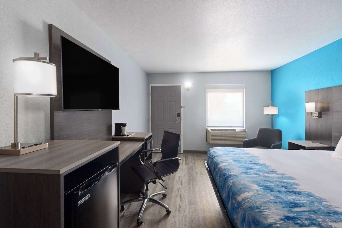 Una habitación de hotel con cama, escritorio, silla, televisor y ventana.