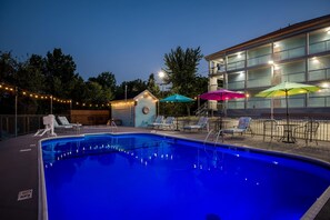 A swimming pool with lounge chairs and umbrellas, surrounded by a building with multiple balconies. - Baymont by Wyndham Branson Thousand Hills (Branson)