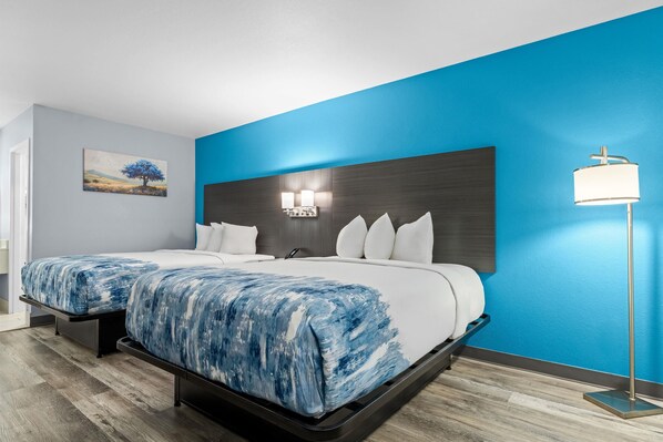 A hotel room with a large bed, a nightstand, a wall-mounted lamp, and a painting.