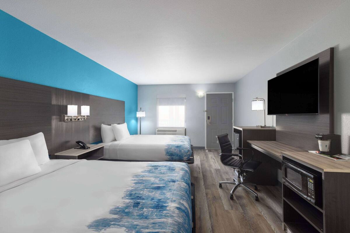 Una habitación de hotel con dos camas, un escritorio con computadora, televisor y microondas.
