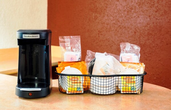 A coffee maker and a basket of packaged food items on a countertop. - Red Roof Inn Albany Airport (Albany)